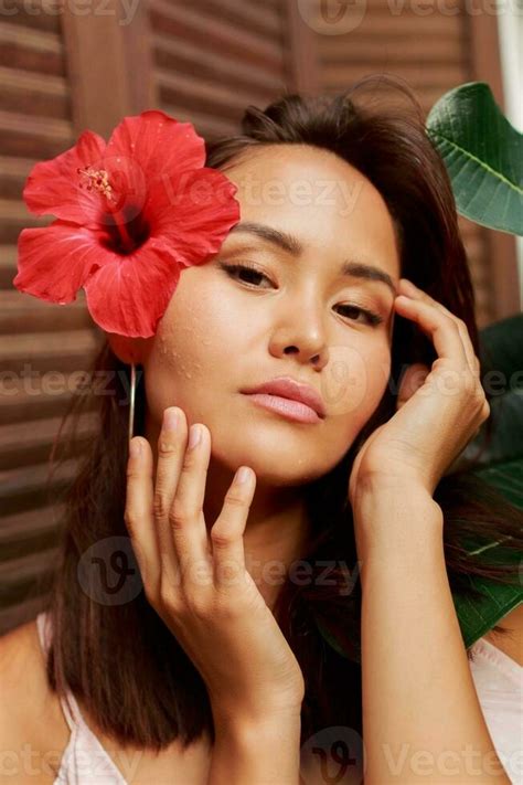 Graceful Asian woman with perfect skin and hibiscus flower in hairs posing over wood wall and ...
