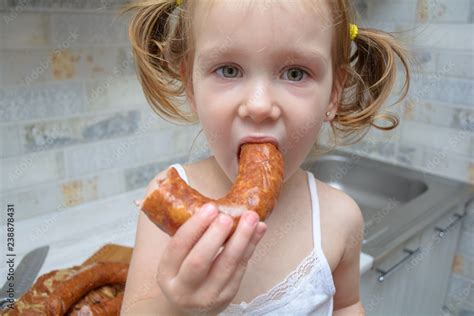 funny hungry baby girl eats smoked sausage and pork ribs in the kitchen Stock Photo | Adobe Stock
