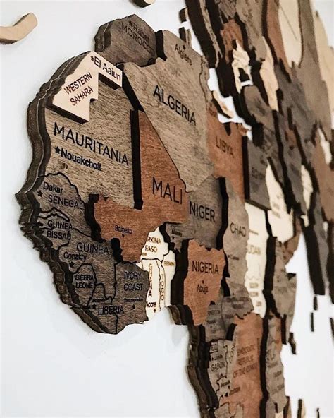 a wooden cutout map of the world on a white wall with words written in different languages