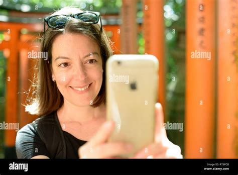 Woman uses smart phone to photograph Torii gates at Shinto shrine Fushimi Inari-taisha, Kyoto ...