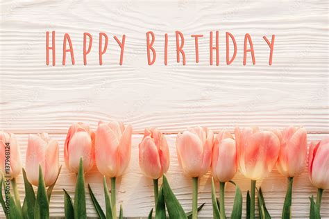 happy birthday text sign on pink tulips on white rustic wooden background flat lay. spring top ...