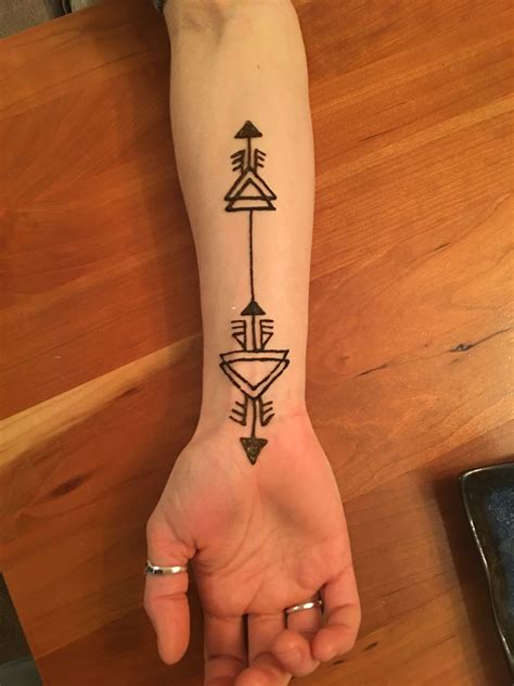 a woman's arm with an arrow tattoo on the left side of her hand