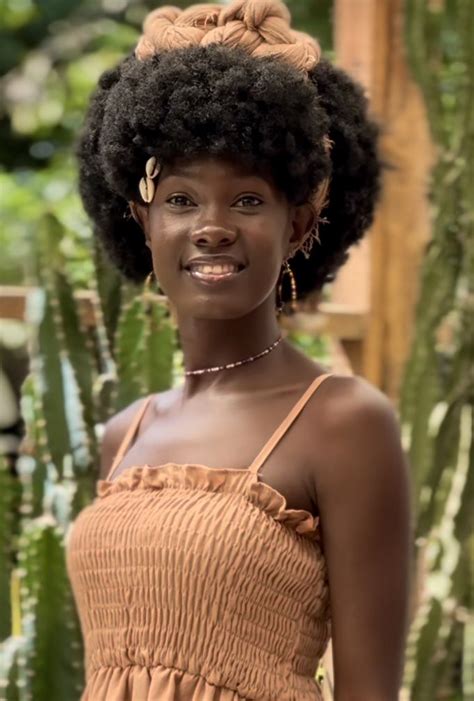 a woman with an afro standing in front of some cactus plants and smiling at the camera