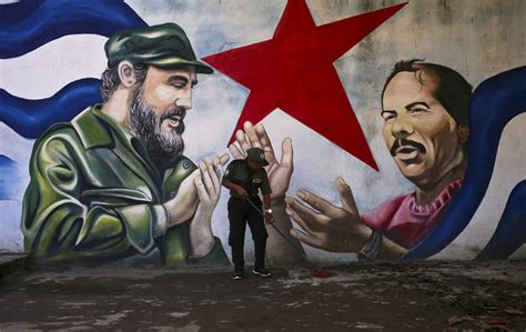 A woman sweeps the Cuba Plaza backdropped by a mural depicting Cuba’s ...