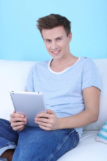 Chico sentado en el sofá con tableta electrónica sobre fondo azul. | Foto Premium