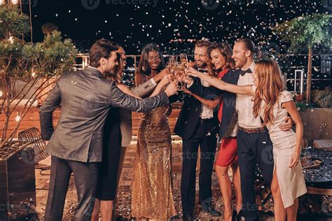 grupo de pessoas felizes em trajes formais brindando com champanhe com confetes voando ao redor ...