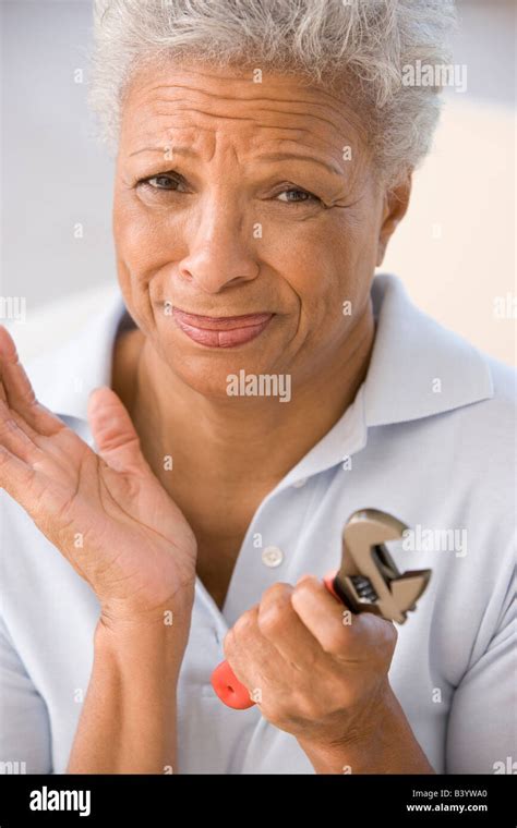 Woman holding wrench looking unsure Stock Photo - Alamy