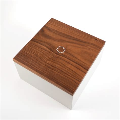 a white box with a wooden lid on a white surface, it has a small metal object in the middle