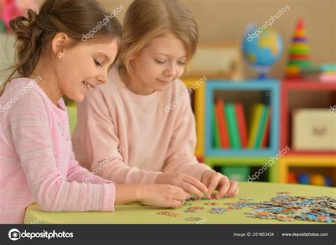 Cute Little Girls Collecting Puzzle Pieces While Sitting Table Stock Photo by ©aletia 281663434