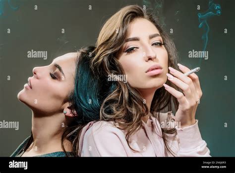 Two young beautiful girls smoking cigarettes at gray background. Harmful and bad habit of young ...
