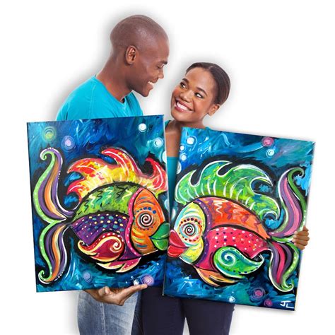 a man and woman holding two colorful fish paintings