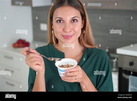 Attractive woman holds bowl of Greek yogurt with granola and smiles at camera with blurred ...