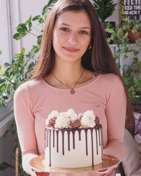 a woman holding a cake with white frosting and chocolate drizzle on it
