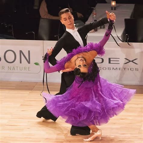 two people dressed in purple and black dancing on a wooden floor