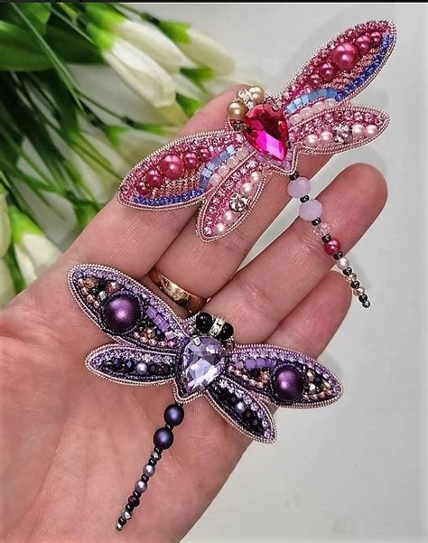 a hand holding a purple dragonfly brooch with pearls and crystals on it ...