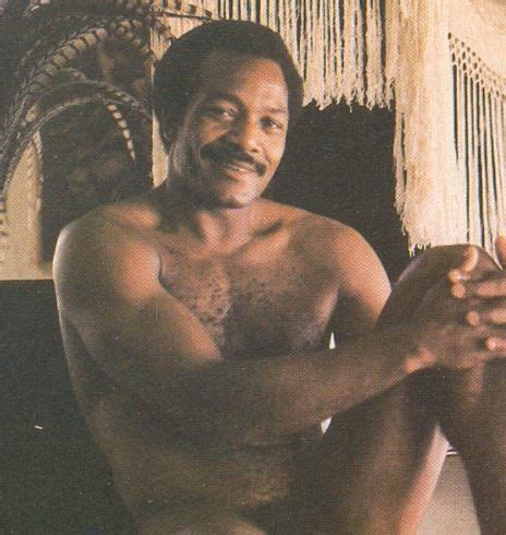 a man with no shirt sitting on the floor next to a hammock and smiling