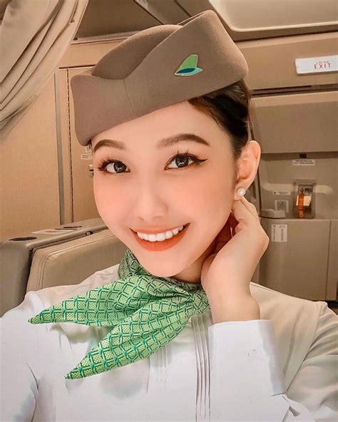 a woman in an airplane cabin wearing a hat and green neck scarf with her hand on her chin