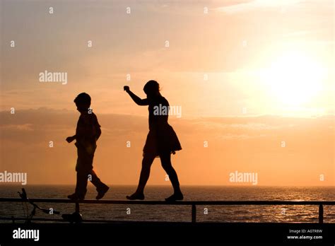 Silhouette of children walking on a railing at sunset by the sea Stock Photo - Alamy