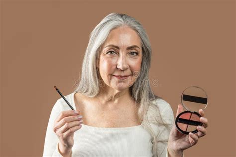 Cheerful Senior European Lady with Gray Hair Shows Cosmetics, Blush or Eye Shadow with Brush ...