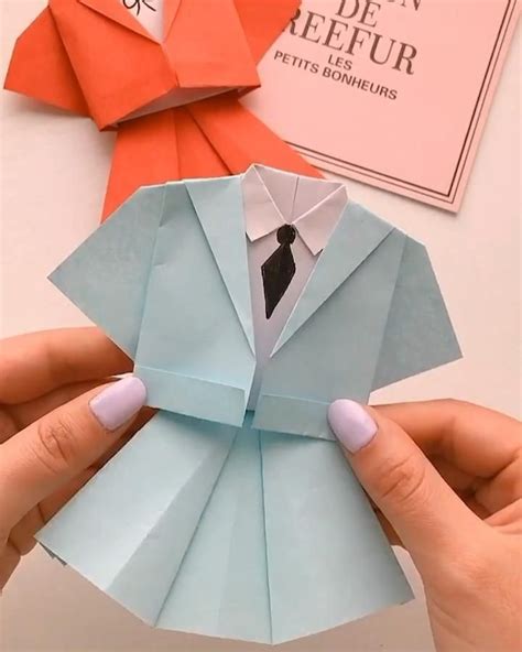 a person is holding an origami shirt and tie in front of some folded paper