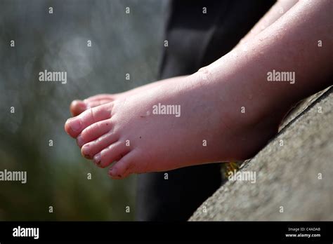 A young toddler child with wet feet after paddling in a river of moving water in the summer time ...