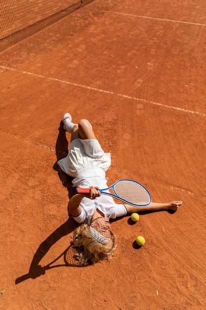 Una joven se acuesta en la cancha de tenis de césped con un traje ...