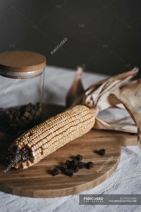 Dried corn on cob placed on wooden board near jar with brown spice on