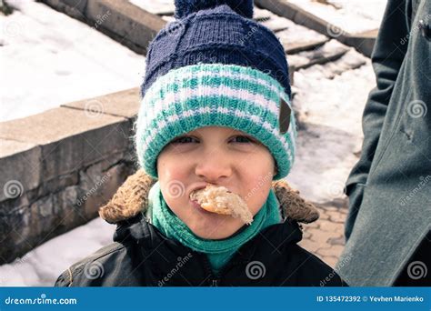 Мальчик с хлебом в его рте Одетый в зиме Он смотрит в камеру Стоковое ...
