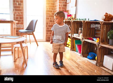 Beautiful toddler boy standing at kindergarten with lots of toys Stock
