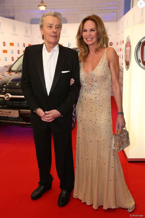 an older man and woman standing on a red carpet in front of a black car