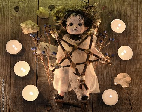 Scary voodoo doll with candles, pentagram and poison berries on witch table. Occult, esoteric ...