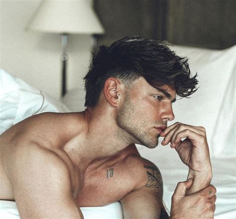 a shirtless man laying on top of a bed next to a white pillow and lamp