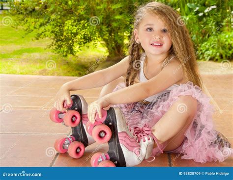 Preschool маленькой девочки сидя в земле касаясь ее конькам ролика, в ...