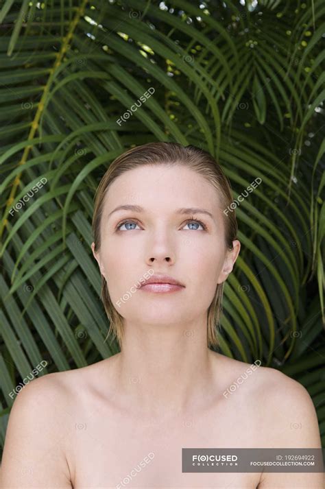 Young woman with bare shoulders looking up with tropical plants in ...