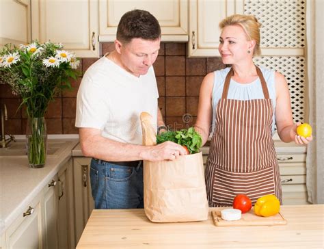 Счастливые пары с сумкой бакалеи бумажной с овощами в кухне Стоковое ...