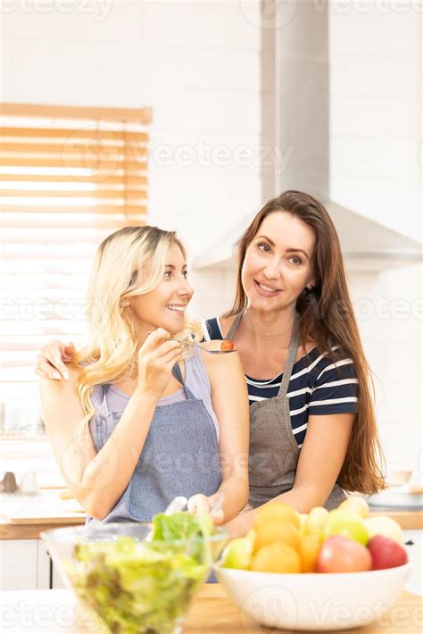 Happy same sex couple feed each other at kitchen. Cheerful LGBTQ