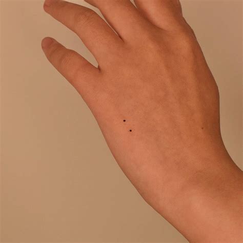 Two dots tattooed on the hand, minimalistic sytle.