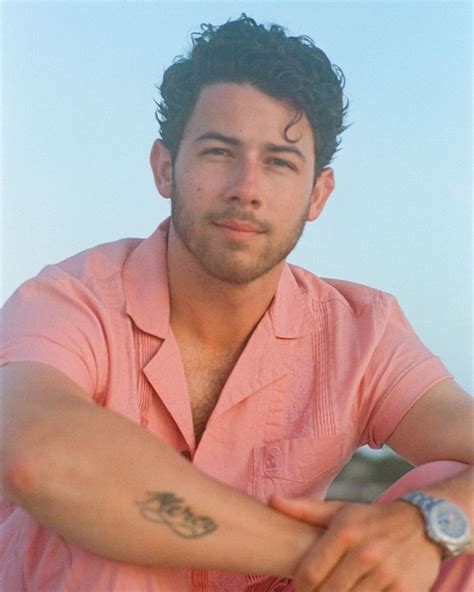 a man with a tattoo on his arm sitting in front of the ocean and looking at the camera