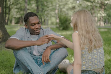 Couple Sitting on the Grass and Man Looking at the Ring on the Female