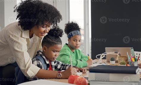 African American female teacher standing with pupils teaching writing