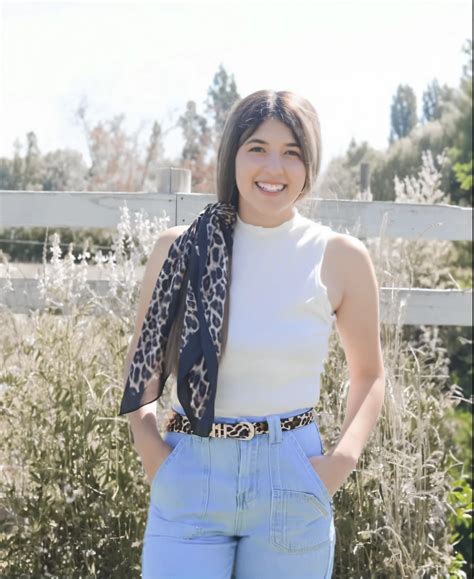 Araffe woman in white top and blue jeans standing in front of a fence