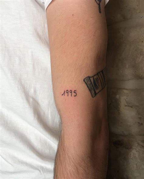 "1995" lettering tattoo located on the upper arm.