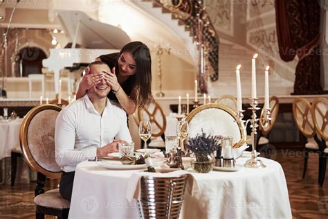 Smiles while girl covers his eyes. Beautiful couple have romantic