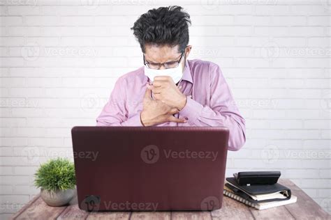 young asian man coughing  sneezes  sited  desk  stock