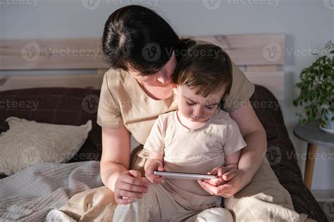 mamá y su pequeño hijo sentar en el cama y acecho dibujos animados en