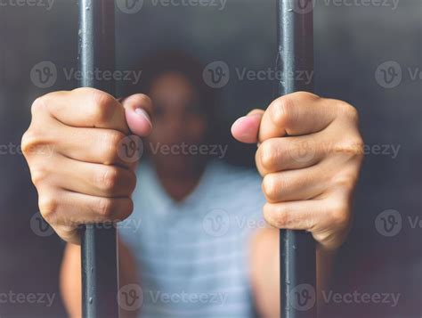 A close-up photo of a persons hands gripping the bars of a prison cell
