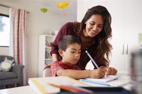 Mother Helping Son With Homework Sitting At Desk In Bedroom - MAEC, Inc.