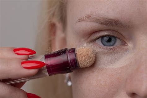 A Young Blonde Woman with Freckles Applies Concealer on Her Face Under ...