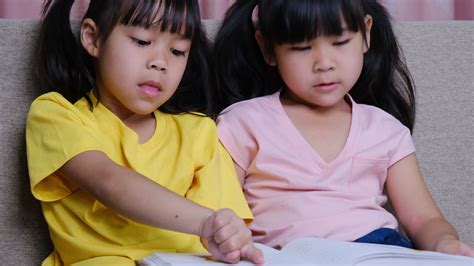 Cute Asian sisters reading a book lying on the sofa at home. 6303405