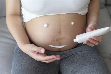 Young pregnant woman applying moisturizing cream on tummy, healthcare